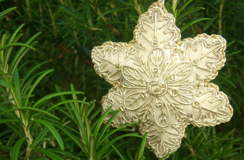 An ivory coloured, fabric Christmas star with gold beading hangs amid green foliage